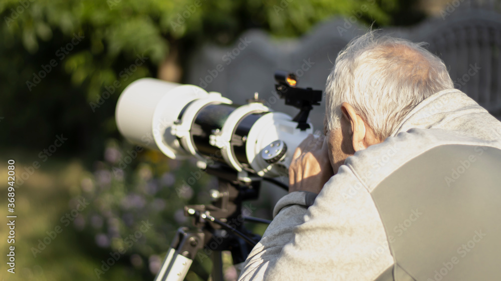 Telescope to nature. A retired man looks at the moon through a telescope. Retired hobby. Blurred background.