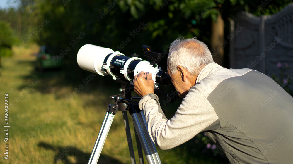 Telescope to nature. A retired man looks at the moon through a telescope. Retired hobby. Blurred background.