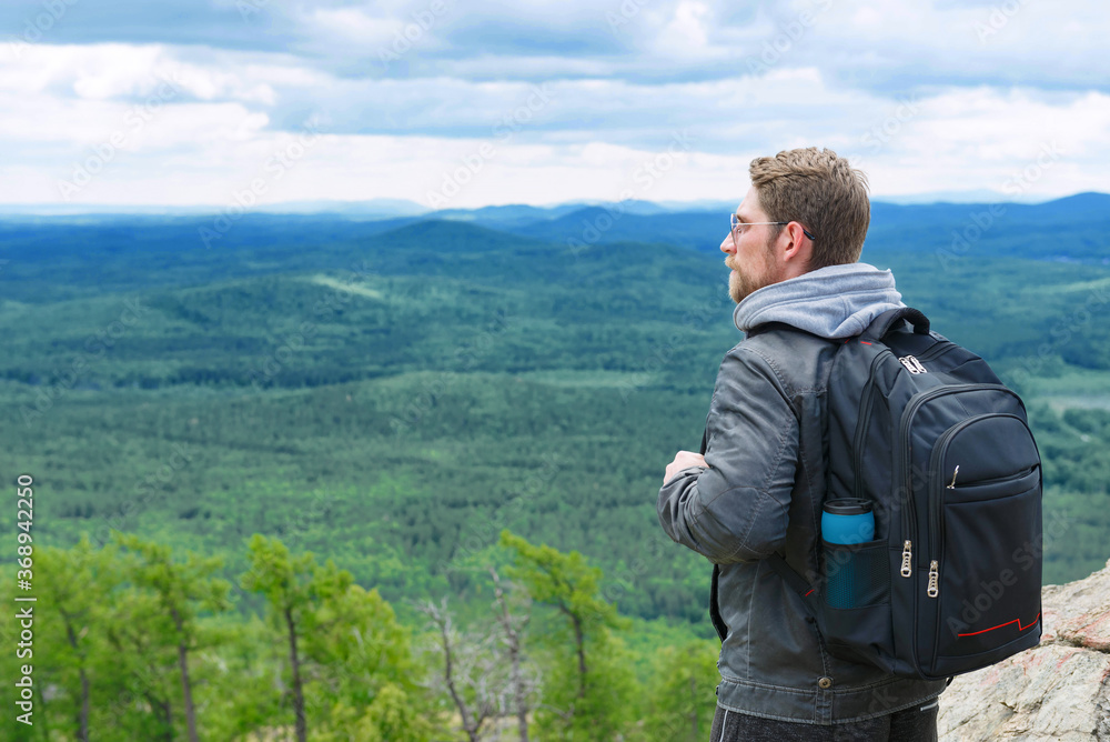 The guy stands on the top of the mountain with a backpack and enjoys the view. The guy stands on the top of the mountain with a backpack and enjoys the view.