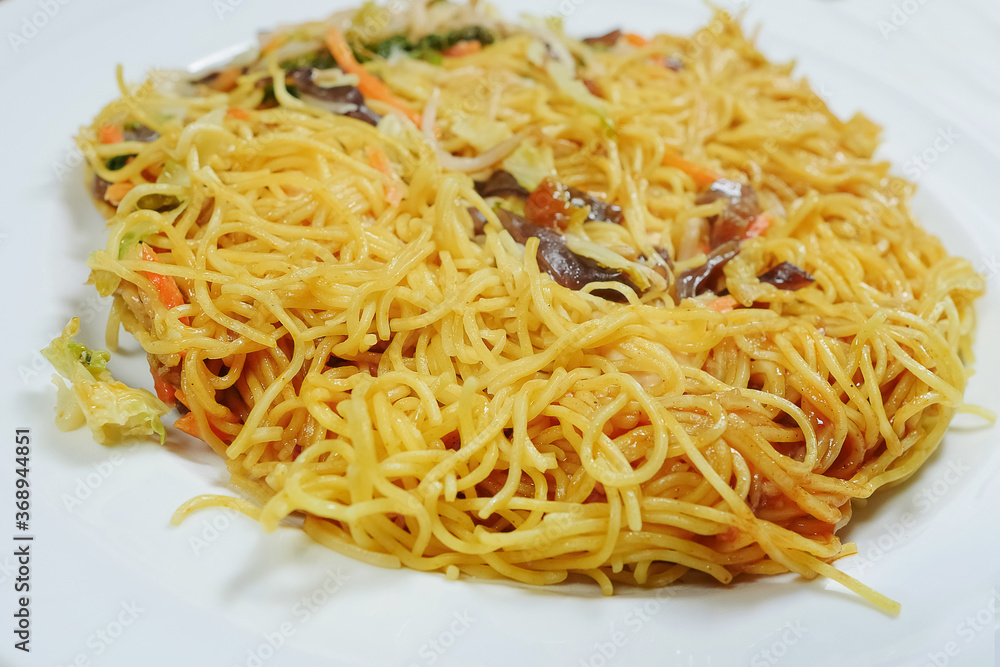 Simple chicken chow mein meal on a white plate and on a wooden table. Chinese stye tasty noodles with sauce and vegetables. Concept dinner, Asian flavor. Simple chicken chow mein meal on a white plate and on a wooden table. Chinese stye tasty noodles with sauce and vegetables. Concept dinner, Asian flavor.