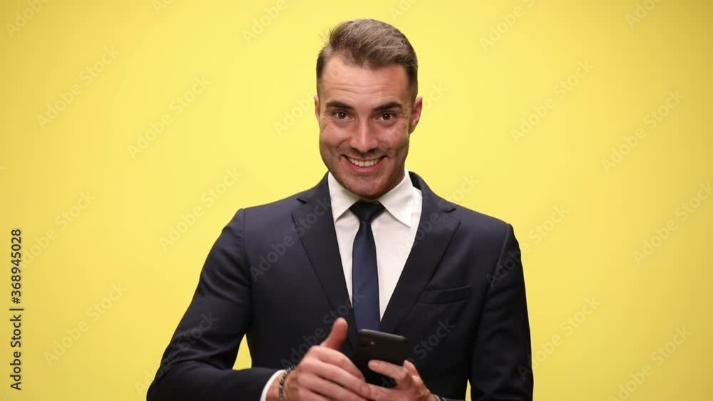 elegant fashion business in suit holding phone reading emails looking up smiling and making thumbs up sign on yellow background elegant fashion business in suit holding phone reading emails looking up smiling and making thumbs up sign on yellow background