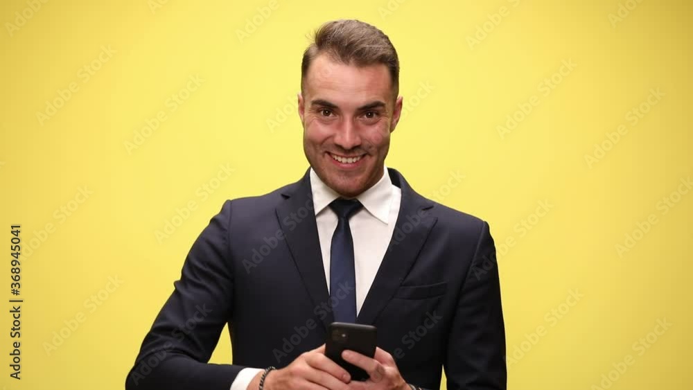 young fashion man in suit holding phone reading messages looking up smiling pointing fingers smiling on yellow background young fashion man in suit holding phone reading messages looking up smiling pointing fingers smiling on yellow background