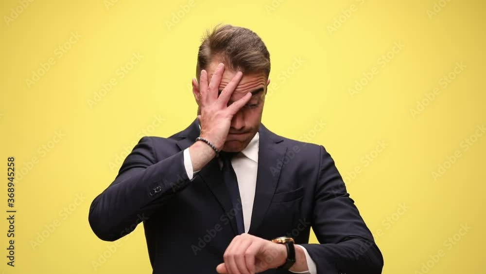upset elegant businessman in suit checking time and realizing it's late, face palming, shaking head and disapproving, covering face with hands and standing on yellow background upset elegant businessman in suit checking time and realizing it's late, face palming, shaking head and disapproving, covering face with hands and standing on yellow background
