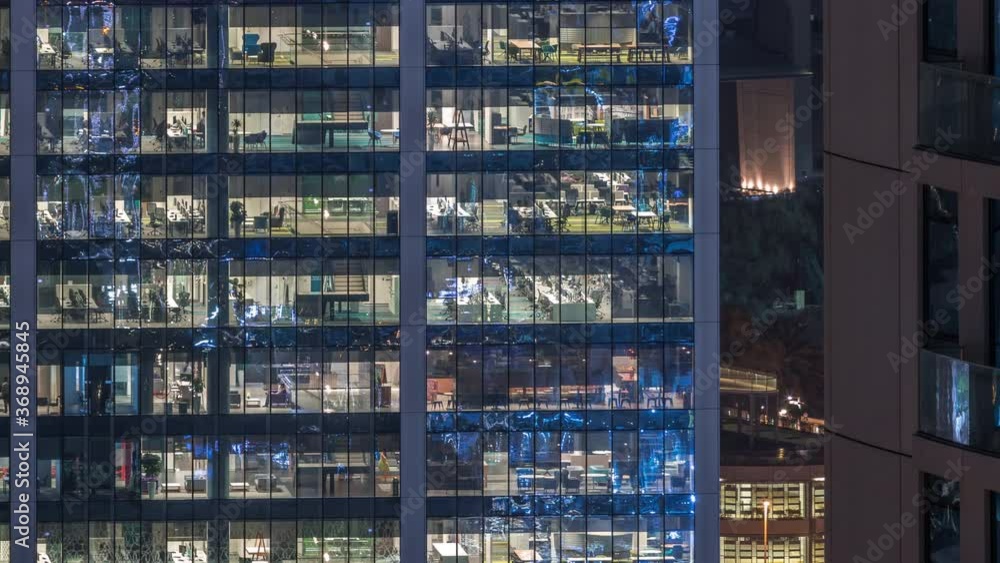 Office building exterior during late evening with interior lights on and people working inside skyscraper night timelapse. Aerial close up view from above with many illuminated windows. Office building exterior during late evening with interior lights on and people working inside skyscraper night timelapse. Aerial close up view from above with many illuminated windows.