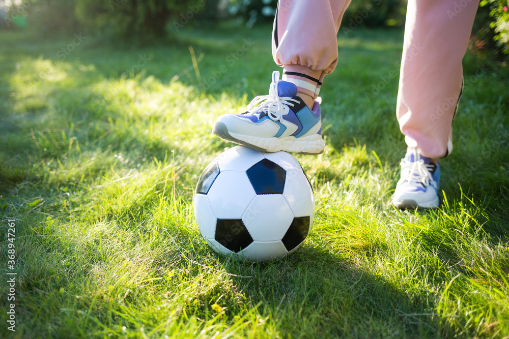 feet in sneakers and soccer ball on grass in sun. children play football. activity sport in summer feet in sneakers and soccer ball on grass in sun. children play football. activity sport in summer