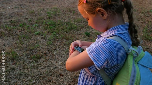 Kid using smartwatch outdoor in park. Child talking on vdeo call on the smartphone. Schoolgirl using touchscreen display on watches browsing internet. Smart wristwatch with GPS tracker.