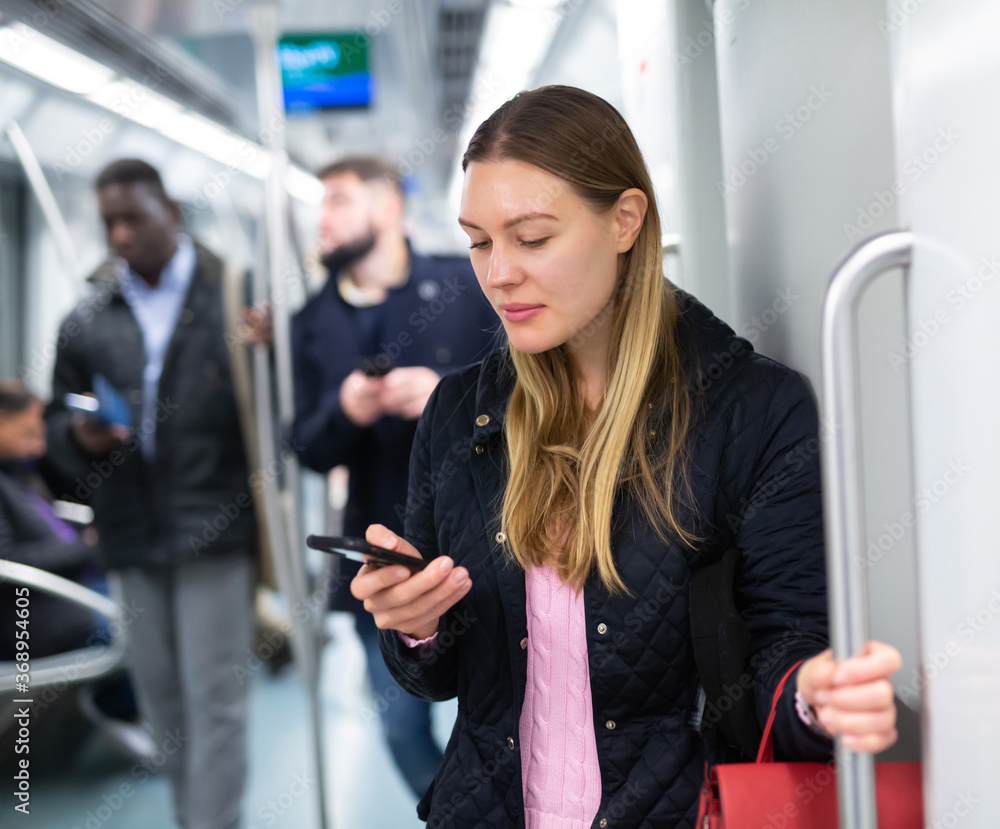 Positive young woman absorbed in her smartphone while traveling in subway car