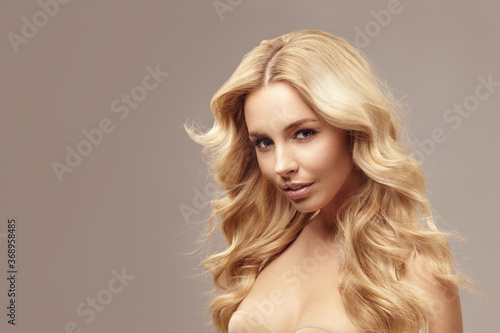 Blonde caucasian woman has long hair, beauty portrait of female face with natural skin on isolated light brown background.