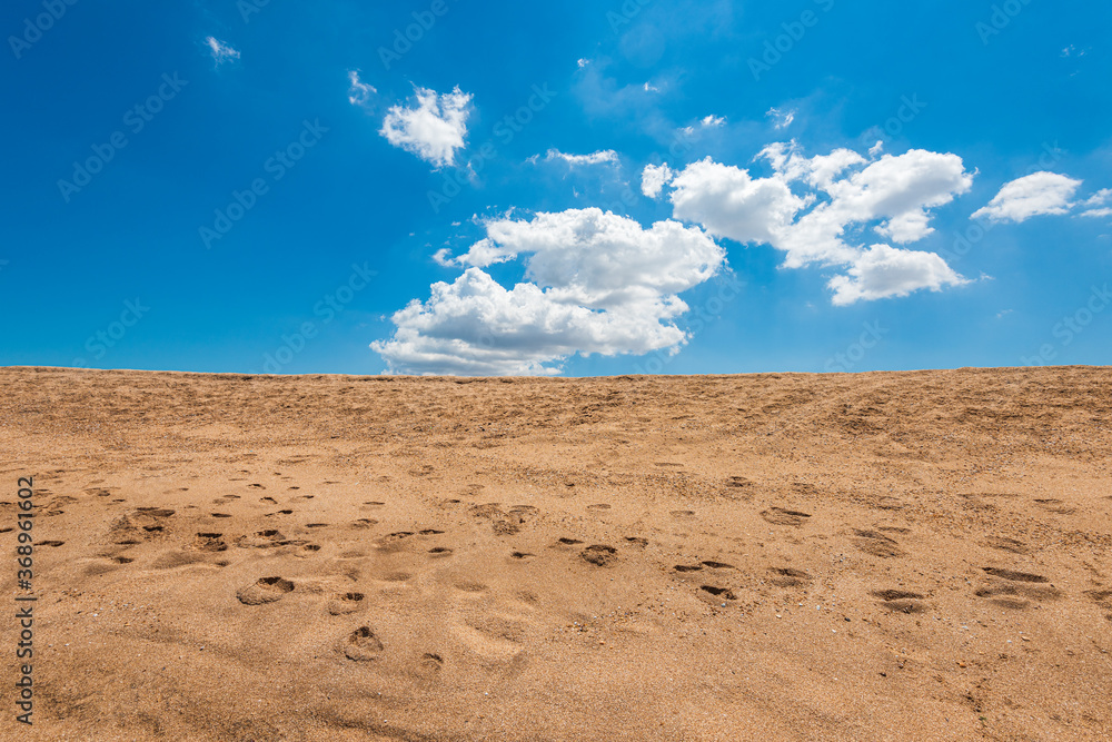 Footprints in yellow sand and blue cloudy sky