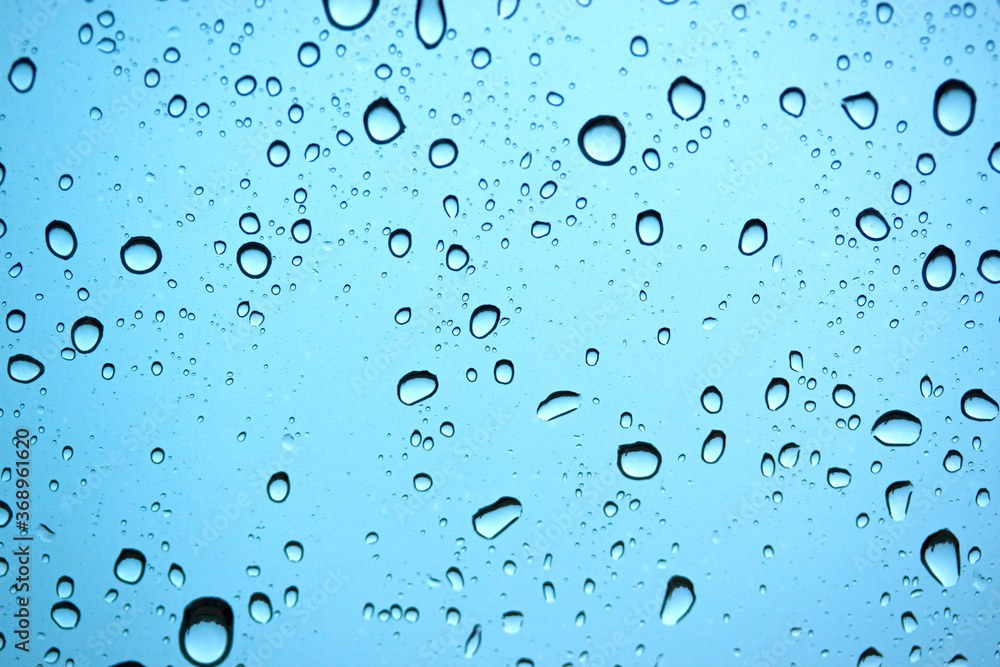 A lot of drops water on car glass in rainy season natural rain on blue background.