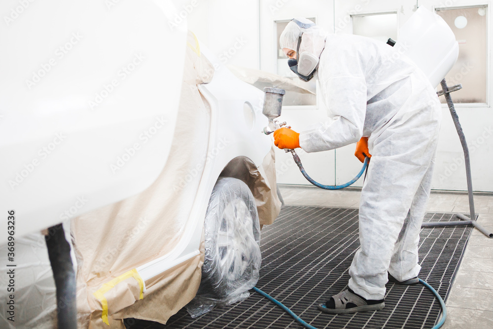 Professional male car painter is painting in garage by airbrush. Man