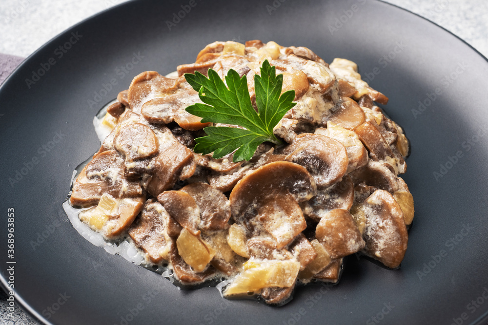 Stewed mushrooms champignons in sauce with sour cream and cheese parsley on a plate. Stewed mushrooms champignons in sauce with sour cream and cheese parsley on a plate.