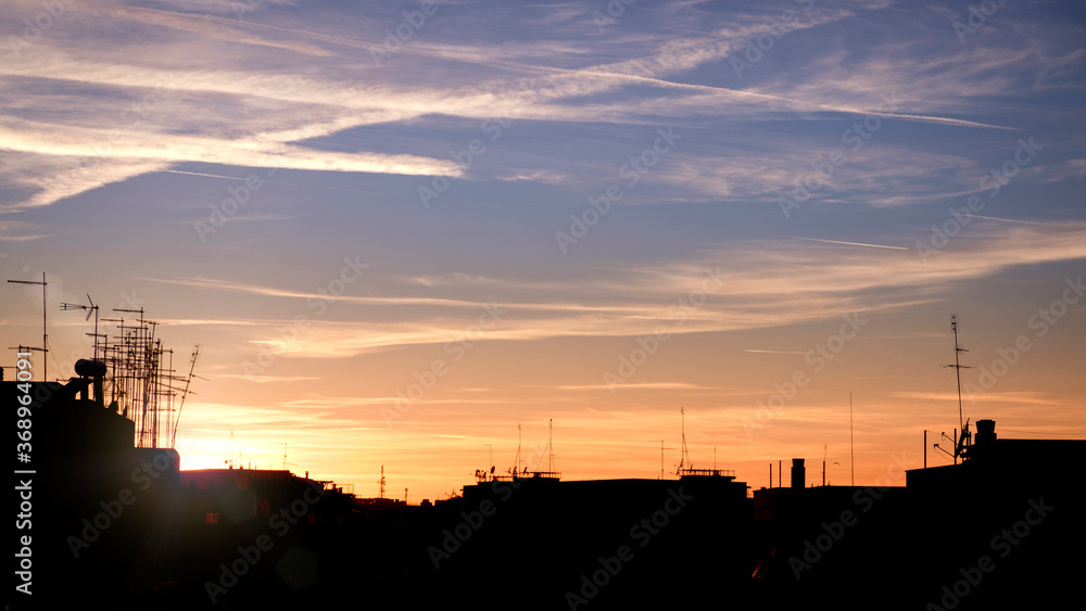 City skyline silhouette at sunset with clouds and trails on the stunning blue and orange sky