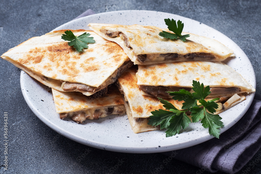 Pieces of quesadilla with mushrooms sour cream and cheese on a plate with parsley leaves. Concrete background close up.