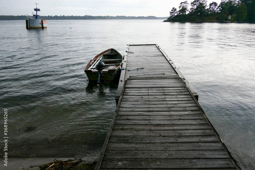 Naklejka premium Sater, Sweden A small dock and a rowboat on Braviken bay in the rain.