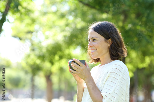 Happy adult woman holding a cup of coffee in a park
