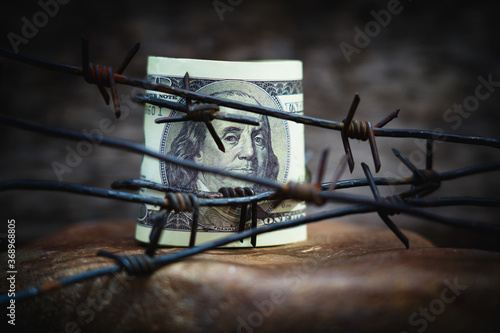 Barbed wire against US Dollar bill as symbol of economic warfare, confrontation, sanctions and embargo busting.