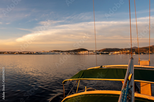 Pink sunrise over the sea and Naoussa coastal village (Paros Island), landscape view from sailing boat with boat canopy in the foreground, and traditional whitewashed houses in the background, Greece.