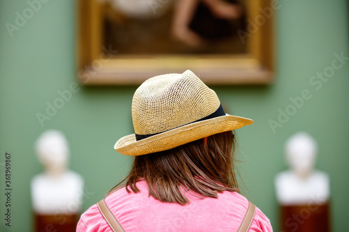 Girl in a hat looks at paintings in a museum