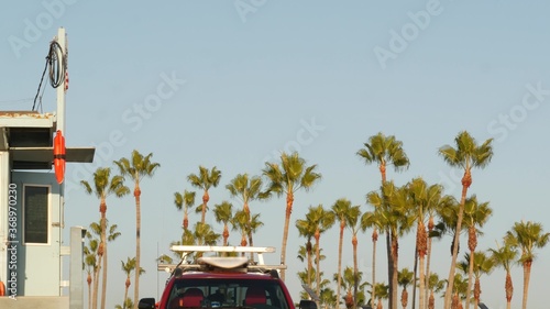 Iconic retro wooden lifeguard watch tower and baywatch red car. Life buoy, american state flag and palm trees against blue sky. Summertime california aesthetic, Santa Monica beach, Los Angeles, CA USA