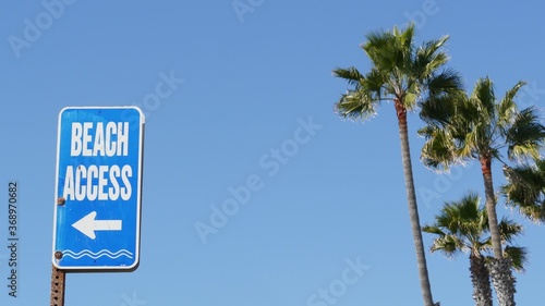 Beach sign and palms in sunny California, USA. Palm trees and seaside signpost. Oceanside pacific tourist resort aesthetic. Symbol of travel holidays and summertime vacations. Beachfront promenade