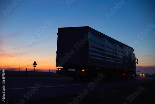 a cargo truck drives on the motorway in the evening against the backdrop of sunset. Truck logistics and transportation concept, copy space for text, business
