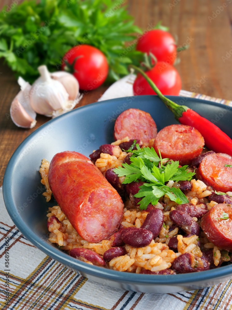 Red beans and rice with sausage in bowl over wooden table, vertical