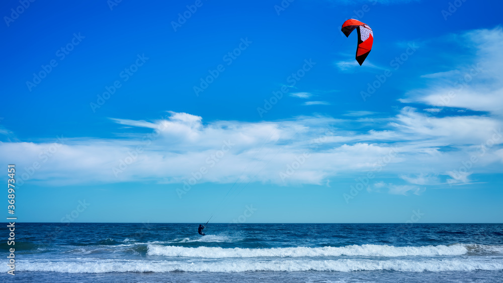 Man kitesurfing or kite boarding sports on Brora beach in the Highlands on a sunny day with blue skies