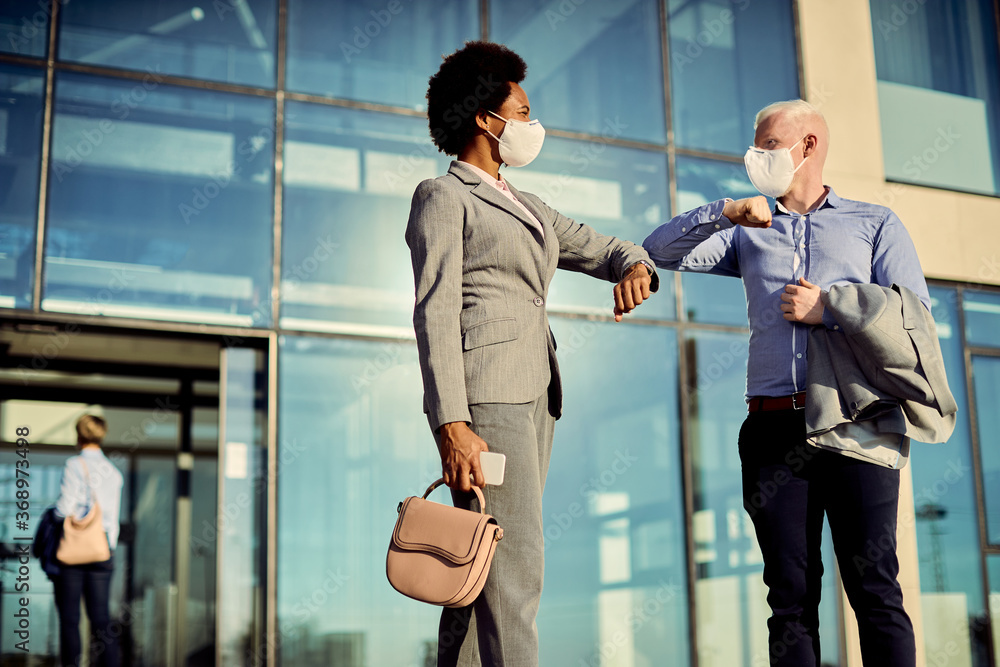 Happy colleagues with face masks elbow bumping while greeting outdoors. Happy colleagues with face masks elbow bumping while greeting outdoors.