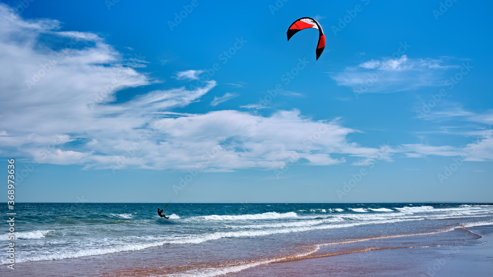 Man kitesurfing or kite boarding sports on Brora beach in the Highlands on a sunny day with blue skies Man kitesurfing or kite boarding sports on Brora beach in the Highlands on a sunny day with blue skies