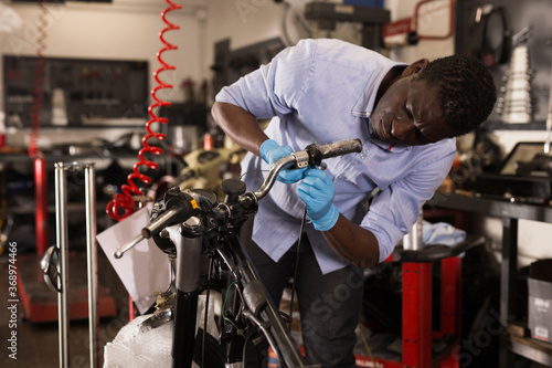 Afro american worker fixing failed motorcycle in workshop. High quality photo