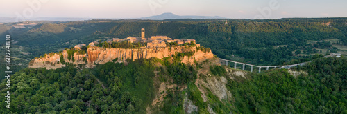 Civita di Bagnoregio. Panoramic, aerial view of Italian ancient village standing on rock plateau, illuminated by setting sun. City on rock over Tiber river valley. Italy.