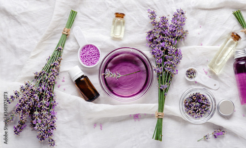Lavender oils, liquids, parfumes, lavender flowers on white fabric. Set skincare spa beauty cosmetic products. Lavender essential oil. Apothecary herbs for aromatherapy. Flat lay long web banner