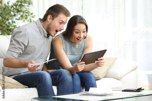 Excited couple checking tablet and receipts at home
