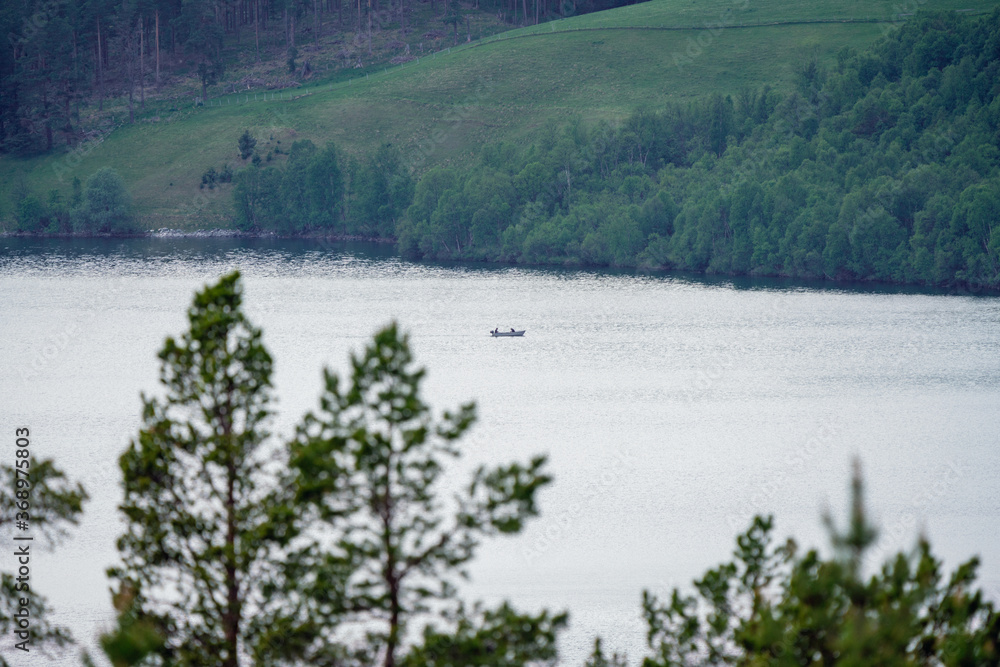 Fishermen in a boat are fishing on the river of Atna in Norway, photographed with telezoom. Nature, lifestyle and landscape concept.