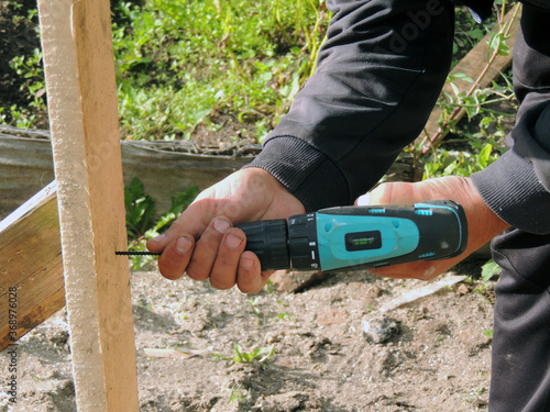 A worker screws a screw driver into a Board to attach it to another Board. A man makes a design on his site. Drilling in wooden boards. 