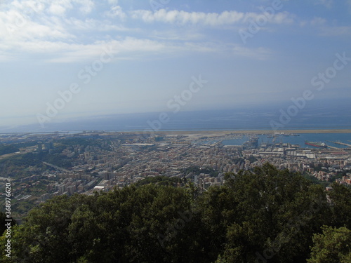 Genova, Italy – 07/30/2020: Beautiful scenic aerial view of the city, port, dam, sea, Cristoforo Colombo airport runway, containers shipping terminal, Pra, Voltri, and Sestri promontory from Monte Gaz