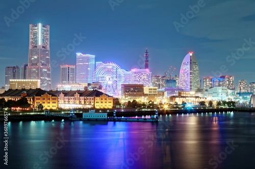 Vibrant night scenery of Yokohama Minatomirai Bay Area with Landmark Tower among skyscrapers in background  a giant Ferris wheel in an amusement park   reflections of colorful city lights on water