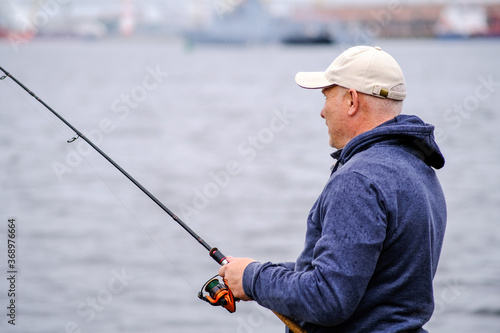 A fisherman in a baseball cap with a fishing rod in his hands smiles. Concept of healthy outdoor recreation.