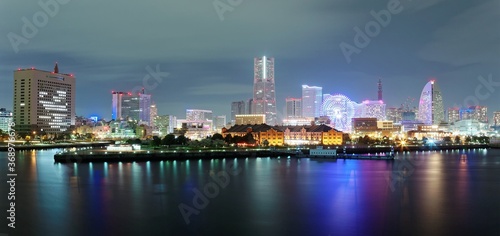 Beautiful night scenery of Yokohama Minatomirai Bay area with high rise buildings in the background, a giant Ferris wheel in Cosmo World Amusement Park & colorful reflections of city lights on water