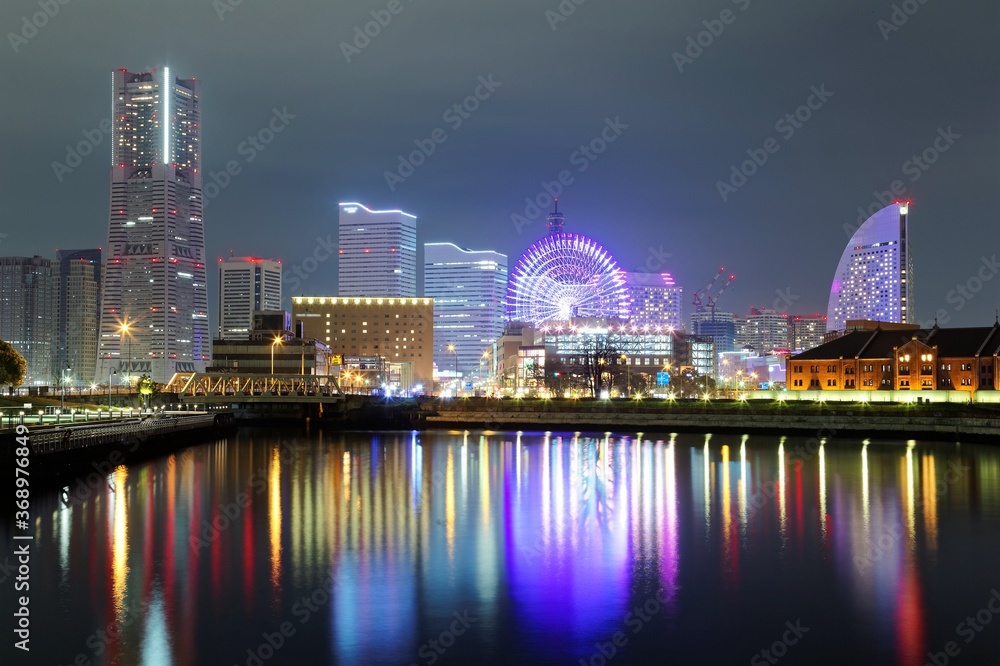 Naklejka premium Beautiful night scenery of Yokohama Minatomirai Bay area with high rise buildings in the background, a giant Ferris wheel in Cosmo World Amusement Park & colorful reflections of city lights on water