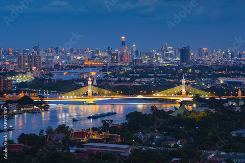 Aerial view of Maha Chesadabodindranusorn Bridge or Nonthaburi Bridge crossing Chao Phraya River and Bangkok skyline, Thailand. Urban city and downtown with skyscraper buildings at night photo