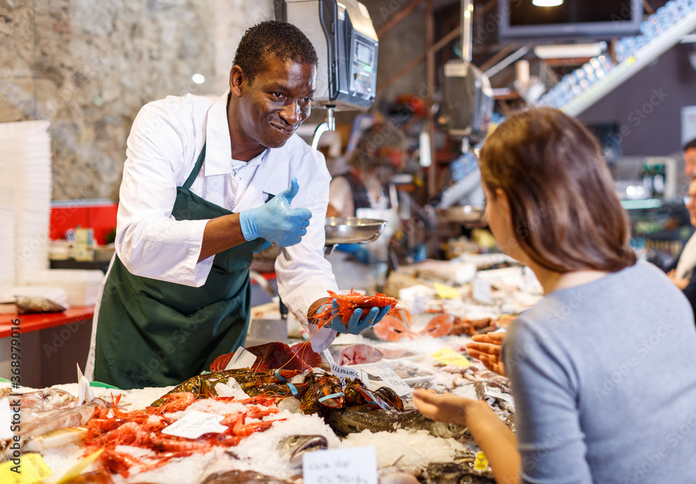 Portrait of salesman in apron helping girl choose shrimps at fish store