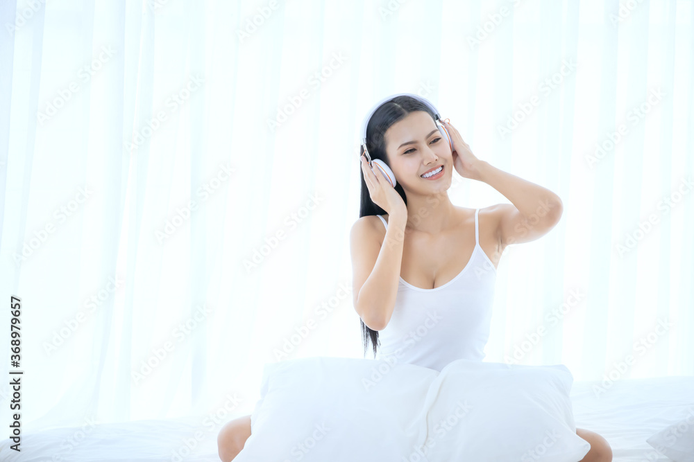 a beautiful Asian woman wake up and sitting on white bed in the bedroom, sexy girl listen to music for relaxing in the morning a beautiful Asian woman wake up and sitting on white bed in the bedroom, sexy girl listen to music for relaxing in the morning