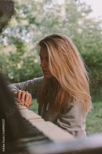 Portrait sad beautiful blondhair girl sitting on piano in the park. 