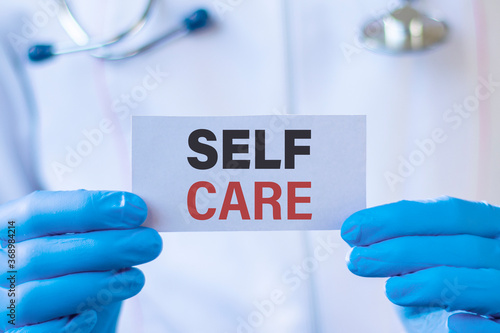 Doctor's hands in blue gloves with a white card. Conceptual words SELF CARE. Medical concept.
