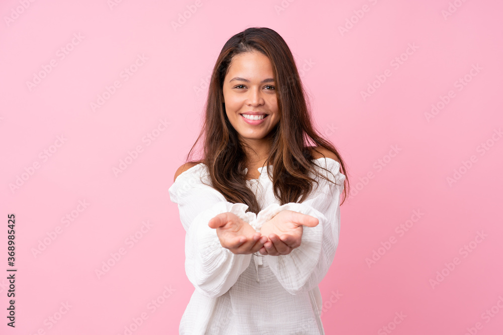 Young Brazilian girl over isolated pink background holding copyspace imaginary on the palm to insert an ad Young Brazilian girl over isolated pink background holding copyspace imaginary on the palm to insert an ad