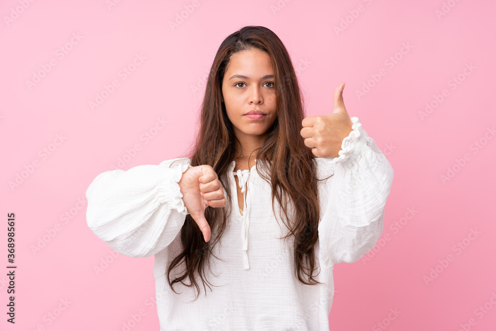 Young Brazilian girl over isolated pink background making good-bad sign. Undecided between yes or not Young Brazilian girl over isolated pink background making good-bad sign. Undecided between yes or not