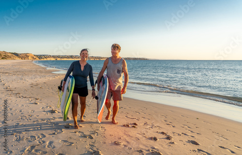Mature couple surfers with surfboard having fun on empty remote beach enjoying outdoors lifestyle