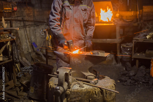 Professional blacksmith forging molten metal on anvil at smithy, workshop. Handmade, craftsmanship and blacksmithing concept